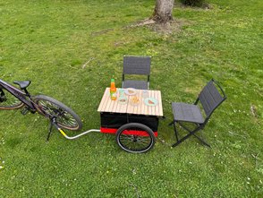Der Fahrradanhänger Hmax light von Hinterher mit einer Tischplatte aus Holz als Picknicktisch im Grünen