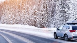 Auto mit Dachbox fährt durch verschneite Winterlandschaft. 