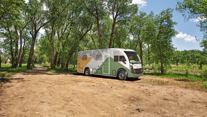 Thor Test Vehicle parkt auf festgestampfter Erde vor hohen grünen Bäumen.