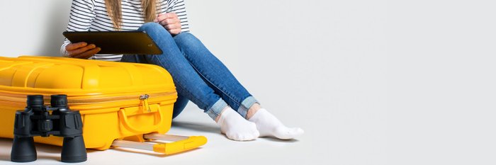 Frau mit Ipad neben einem gelben Koffer.