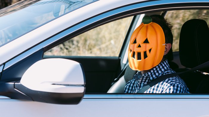 Ein Mann sitzt mit einer Halloween-Maske verkleidet am Steuer eines Autos.