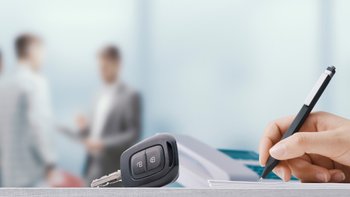 Eine Hand unterschreibt etwas, daneben ein Autoschlüssel.