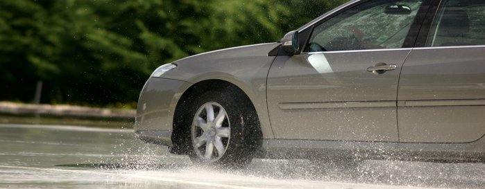 Nahaufnahme eines Autoreifens auf nasser Straße.