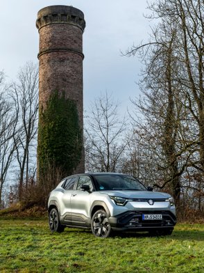 Suzuki eVitara parkt auf einer Wiese vor einem historischen gemauerten Turm.