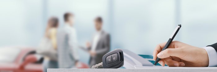 Eine Hand unterschreibt etwas, daneben ein Autoschlüssel.