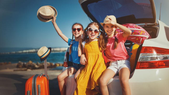 Drei Mädchen sitzen im Kofferraum und freuen sich auf den Urlaub. 