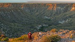 Zwei Wanderer laufen durch eine zerklüftete Tiefebene, dahinter das Meer.