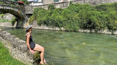 Frau sitzt auf einer Steinmauer am Fluss und kühlt ihre Füße im Wasser.