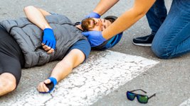 Ersthelfer versorgt verletzten Radfahrer nach Verkehrsunfall. 