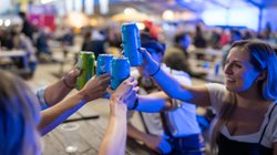 Fünf feiernde Festbesucher stoßen an einem Tisch mit Dosenbier an.