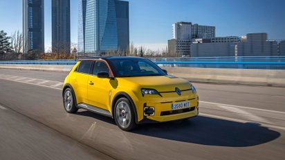 Renault 5 E-Tech fährt auf der Straße einer großen Stadt.